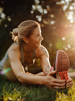 "A woman stretching her legs while smiling, bathed in the warm sunlight of a park."