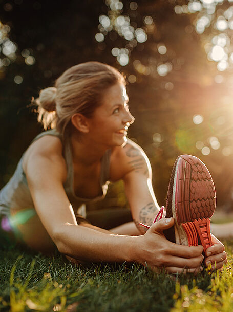 "A woman stretching her legs while smiling, bathed in the warm sunlight of a park."