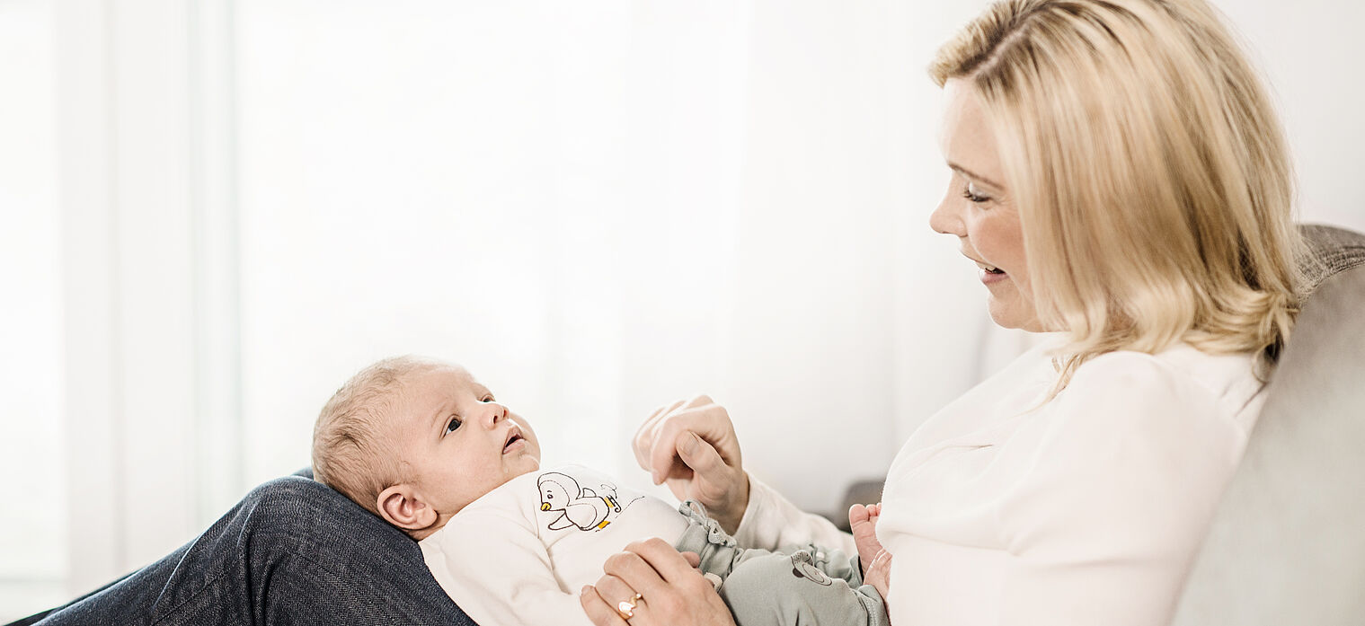 Mother sitting on a couch and looking lovingly at her baby lying on her lap, in a bright and cozy room